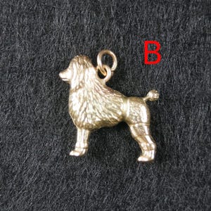 May include: A gold-toned metal charm shaped like a standing poodle dog with textured fur detailing on the head and chest, smooth legs, and a small circular jump ring attached to the top. The letter B is printed in red in the upper right corner.