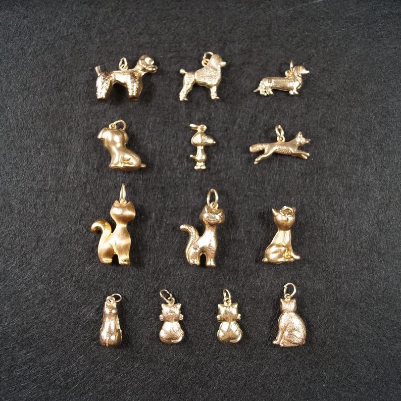 May include: A collection of thirteen gold-toned metal charms shaped like various animals, including dogs and cats. Each charm features a small loop at the top for attachment, with detailed textures representing the fur and features of each animal.