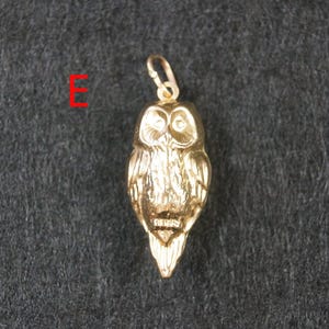 May include: A gold-colored metal owl pendant featuring detailed feather textures and a small circular bail at the top for attachment. The letter E is printed in red to the left of the pendant, which has a polished finish and a distinct beak.