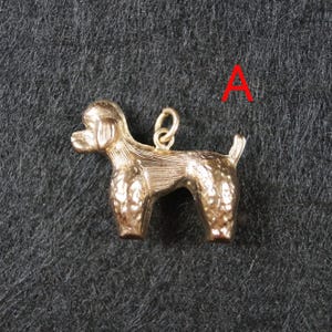 May include: A gold-toned metal charm in the shape of a standing poodle dog, featuring textured fur detailing on the body and a small circular jump ring attached to the back. The letter A is printed in red in the upper right corner of the image.