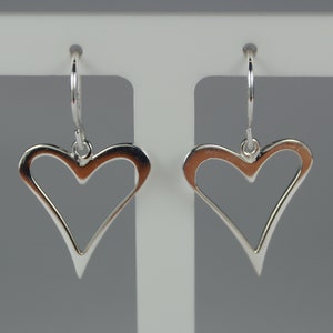 May include: A pair of silver heart-shaped earrings. Each earring features a polished, open heart design suspended from a small hoop. The earrings are displayed against a white background.