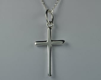 May include: A silver cross pendant on a delicate chain. The cross is a simple, polished design with rounded edges. The necklace is displayed against a soft, neutral background, highlighting the jewelry's shine.