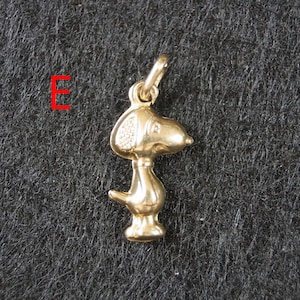 May include: A gold-toned metal pendant shaped like a cartoon dog with a large head, floppy ear, and small tail. The pendant features a small jump ring at the top for attachment. The letter E is printed in red to the left of the dog-shaped charm.