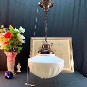 Peut inclure: Suspension luminaire vintage en verre blanc avec un motif décoratif sur la moitié inférieure. Le luminaire est suspendu par une chaîne marron et une chaînette. Le support de plafond est également marron. Une image encadrée et des fleurs sont en arrière-plan.