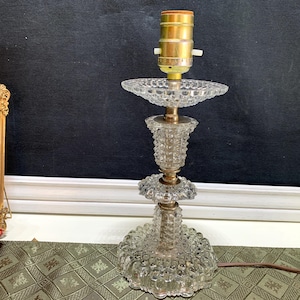 May include: A clear glass table lamp with a textured, bubble-like design. The lamp has a brass-colored base and a standard light bulb socket. The lamp's design includes a round base, a decorative center, and a top plate.