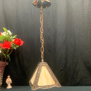 May include: A hanging pendant light fitting featuring a pyramid-shaped shade with cream-coloured glass panels encased in a decorative metallic frame. The lamp is suspended by a matching metal chain connected to a circular ceiling canopy mount.