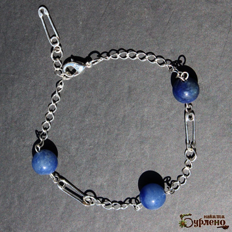 May include: Silver-toned chain bracelet featuring three blue spherical beads. The bracelet design incorporates safety pins as decorative elements, adding a unique touch to the jewelry. The bracelet has a lobster clasp closure.