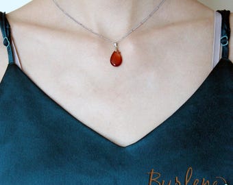 May include: A silver necklace with a teardrop-shaped, reddish-brown pendant. The pendant hangs from a delicate chain. The necklace is displayed against a dark teal background. The text "Burlene handmade jewelry" is visible.