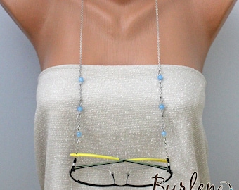 May include: A silver chain with light blue beads holds a pair of black eyeglasses. The eyeglasses have yellow accents and are held in place by the chain. The chain is worn as a necklace and is a stylish way to keep glasses secure.