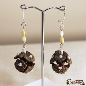 Puede incluir: Un par de pendientes de plata con un dije en forma de piña marrón y cuentas blancas. Los pendientes están colgados de un soporte de plata.