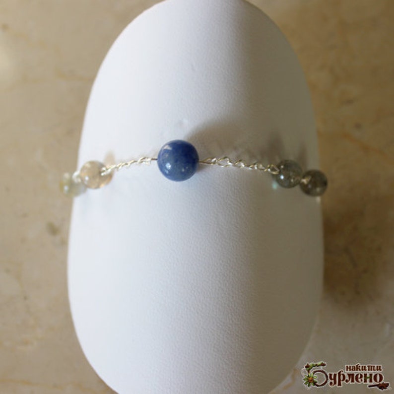 K&ouml;nnte beinhalten: Ein silbernes Kettenarmband mit blauen, grauen und wei&szlig;en Edelsteinperlen.