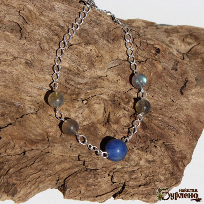 K&ouml;nnte beinhalten: Ein silbernes Kettenarmband mit blauen und grauen Edelsteinperlen. Das Armband hat einen silbernen Verschluss.