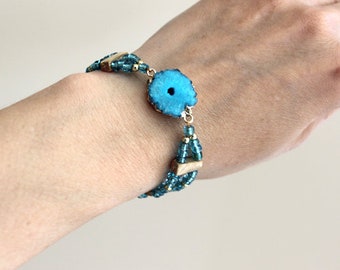 Puede incluir: Un brazalete de ágata azul con detalles dorados y cuentas de cristal azul.