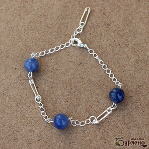 May include: A silver bracelet featuring three blue spherical beads. The bracelet is made with a chain and safety pin links. The clasp is silver. The bracelet is on a brown surface.