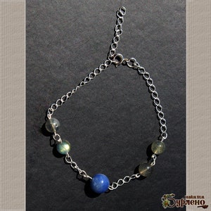 K&ouml;nnte beinhalten: Ein silbernes Kettenarmband mit einem blauen Edelstein und gr&uuml;nen Edelsteinen. Das Armband hat einen Karabinerverschluss.
