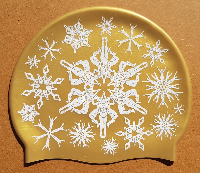 May include: A gold-coloured swimming cap with a white snowflake design. The snowflakes are made up of stylised figures of people in a circle.