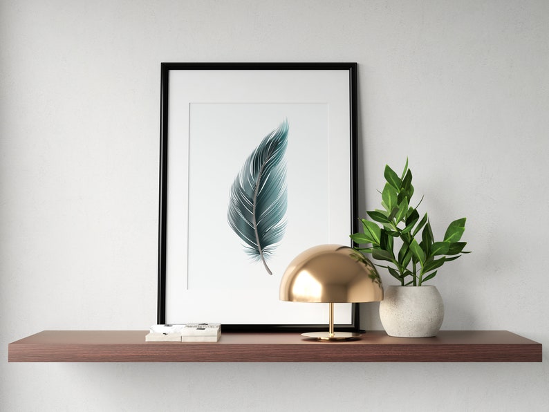 May include: A framed print of a teal blue feather on a white background. The print is on a shelf with a gold lamp and a potted plant.