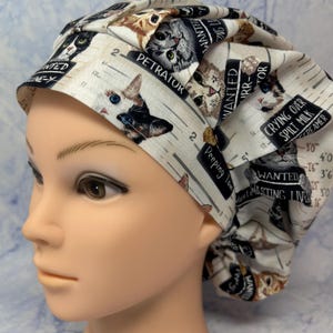 May include: A white and beige patterned scrub cap featuring various cat illustrations and text. The cap has a humorous theme with phrases like "Wanted" and "Crying Over Spilt Milk". The cap is designed to fit comfortably.