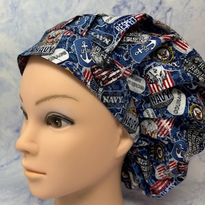 May include: A blue scrub cap with a navy theme. The cap features various patches with the word "NAVY", anchors, and American flags. The text "RESPECT", "COURAGE", and "HONOR" are also visible on the cap.
