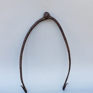May include: A rusty metal tool with two curved arms and a pointed end. The tool is shaped like a pair of tongs.