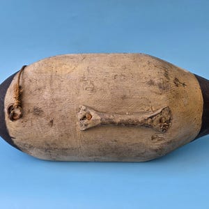 K&ouml;nnte beinhalten: Ein Vintage-Entenk&ouml;der, bemalt in Beige- und Schwarzt&ouml;nen, vor blauem Hintergrund. Der h&ouml;lzerne K&ouml;der hat ein verwittertes Aussehen, mit einer kleinen Schlaufe und einem Metallansatz. Ein klassisches Dekorationsst&uuml;ck.
