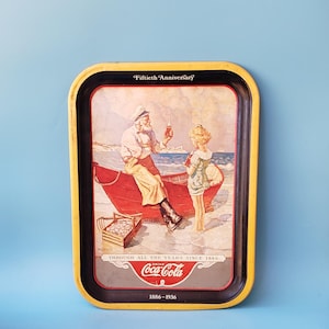 May include: A vintage Coca-Cola metal tray featuring a colorful illustration of two people in a red boat on a beach. The tray has a yellow border and black interior. The text "Fiftieth Anniversary" is printed in black at the top of the tray. The text "Through all the years since 1886" is printed in black at the bottom of the tray. The Coca-Cola logo is printed in red and white with the text "Drink Coca-Cola" and "1886-1936" printed in black.