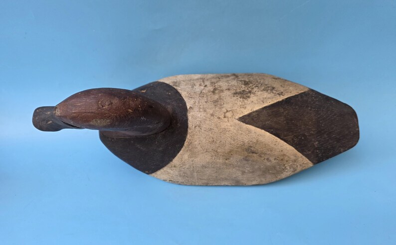 K&ouml;nnte beinhalten: Ein Vintage-Holzentenk&ouml;der, bemalt in Braun-, Schwarz- und Cremet&ouml;nen. Der Entenkopf ist dunkelbraun, mit einem schwarzen und cremefarbenen K&ouml;rper. Der K&ouml;der ist so konzipiert, dass er auf dem Wasser schwimmt und andere Enten anlockt. Ein klassisches St&uuml;ck Volkskunst.