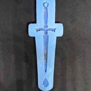 Könnte beinhalten: Eine hellblaue Silikonform zum Herstellen eines Harz-Dägers als Anhänger. Die Form zeigt ein detailliertes Design eines Dolches mit einer tropfenförmigen Basis.