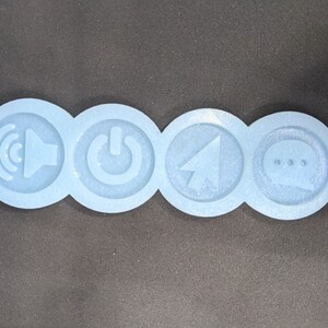 Può includere: Quattro stampi rotondi in silicone con icone in rilievo: un altoparlante con onde sonore, un pulsante di accensione, una freccia del cursore e un fumetto con tre punti.