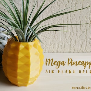 May include: A yellow pineapple-shaped air plant holder with a geometric design. The holder is made of plastic and has a smooth, glossy finish. The text "Mega Pineapple Air Plant Holder" is written below the holder. The text "more colors available!" is written below the text.