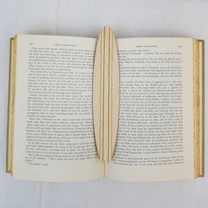 May include: An open book with a wooden bookmark. The book is titled "Great Expectations" and the pages are filled with text. The bookmark is a light brown color and has a smooth, polished surface.