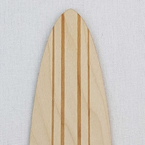 May include: Close-up of the top of a wooden surfboard with a light brown wood grain and five thin, dark brown stripes running vertically down the length of the board.