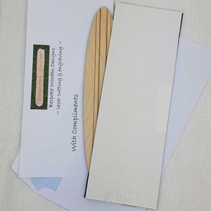 May include: A wooden surfboard bookmark with a natural wood finish and three brown stripes. The bookmark is on a white background with the text "With Compliments" and "Bespoke Wooden Designs - laser cutting & engraving - Imagination Creations".