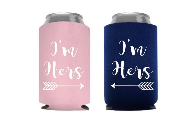 May include: Two can coolers, one pink and one navy blue, each with the text "I'm Hers" in white script, accompanied by a white arrow graphic. The coolers are designed to keep beverages cold.