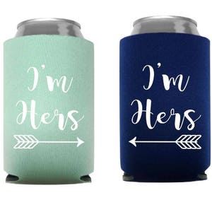 May include: Two can coolers, one mint green and one navy blue, with the text "I'm Hers" in white script. Each cooler has a white arrow pointing towards the other. The coolers are designed to keep beverages cold.