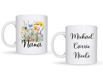 May include: Two white ceramic mugs. One mug features a floral design with the word "Nana" in black script. The other mug has the names "Michael", "Carrie", and "Nicole" in black script.