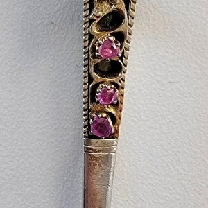 May include: A silver and gold brooch with a cluster of pink gemstones in the shape of a flower. The brooch has a long, pointed pin.