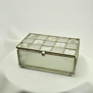 May include: A silver-toned glass box with a frosted glass interior and a grid pattern. The box has a hinged lid and clear crystal accents.