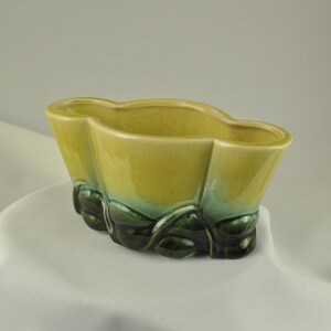 May include: A yellow and green ceramic planter with a scalloped rim and a leafy design. The planter is oval shaped and has a glossy finish.