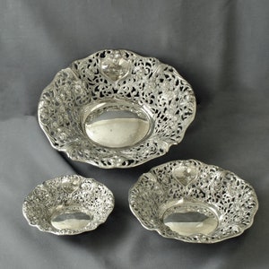 May include: Three silver bowls with intricate floral designs. The bowls are nested together, with the largest bowl on the bottom and the smallest bowl on top.
