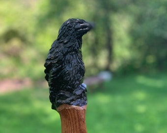 May include: A walking stick with a black crow carved on the top. The stick is made of wood and has a natural brown color.