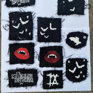 May include: A collection of 10 black fabric patches with white designs. The patches feature various designs, including bats, lips, and the words "Motionless In White" and "IX".