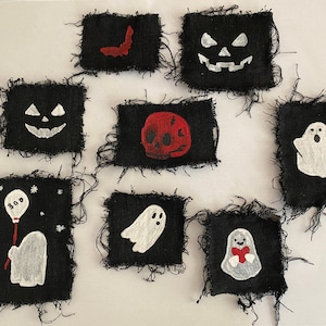May include: Eight black fabric patches with various Halloween-themed embroidery designs. The designs include a ghost holding a balloon, a ghost with a heart, a skull, a pumpkin, a bat, and two ghosts with open mouths.