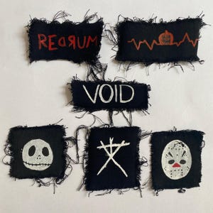 Peut inclure: Cinq patchs en tissu noir avec des broderies blanches et rouges. Les patchs présentent les mots "VOID", "REDRUM" et un "X" stylisé. Un patch a une citrouille et un graphique de battement de cœur. Le dernier patch a un visage blanc ressemblant à Jack Skellington.