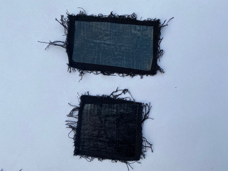 May include: Two black fabric patches with frayed edges. The patches have a clear adhesive backing.