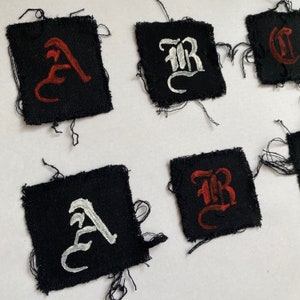 May include: Five black fabric patches with white and red embroidered letters. The letters are in a stylised font and spell out "A", "B", "R", and "C".