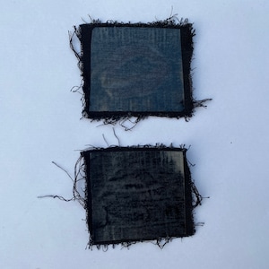 May include: Two black fabric patches with frayed edges. The patches are rectangular and have a textured surface.