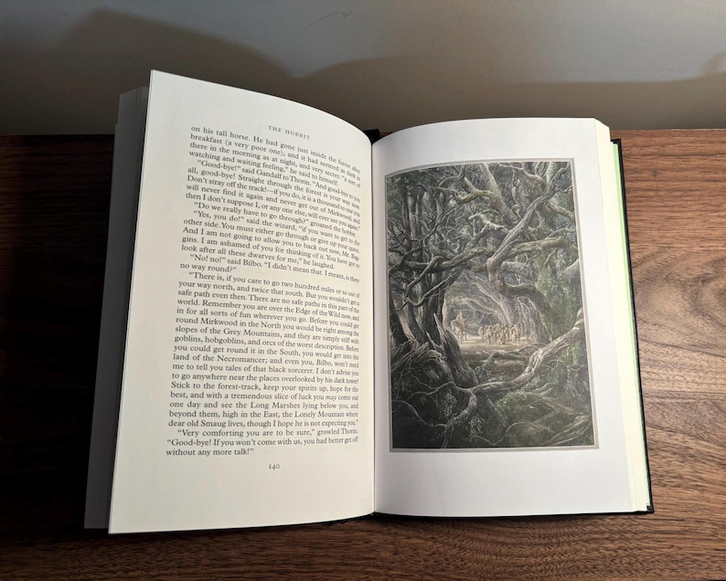 Op de afbeelding: Een open boek met tekst en een illustratie van een bos. Het boek heeft een zwarte kaft en een groene rug, en ligt op een houten oppervlak.