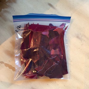 Puede incluir: Una bolsa de pl&aacute;stico transparente llena de trozos de vidrio rojo oscuro de forma irregular. La bolsa est&aacute; sellada con una cremallera azul y blanca y etiquetada "1 lb" con un rotulador negro. Piezas para manualidades.