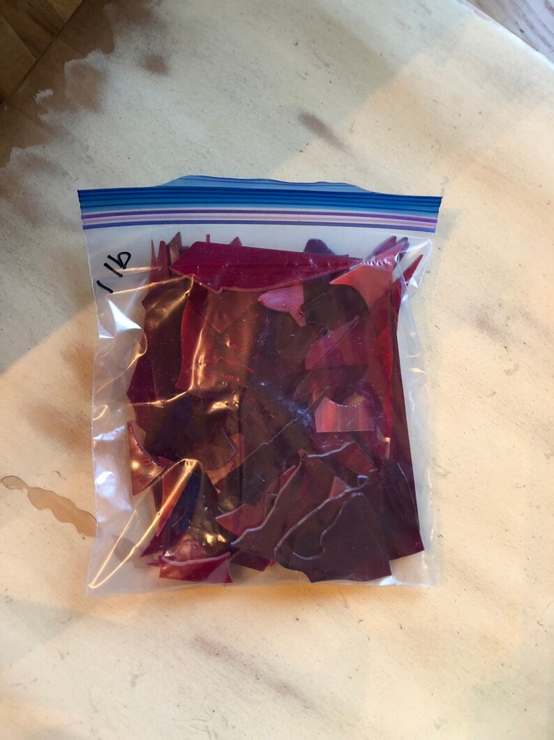 Puede incluir: Una bolsa de pl&aacute;stico transparente llena de trozos de vidrio rojo oscuro de forma irregular. La bolsa est&aacute; sellada con una cremallera azul y blanca y etiquetada "1 lb" con un rotulador negro. Piezas para manualidades.